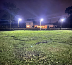 Three bright solar street lights illuminate a large grassy area